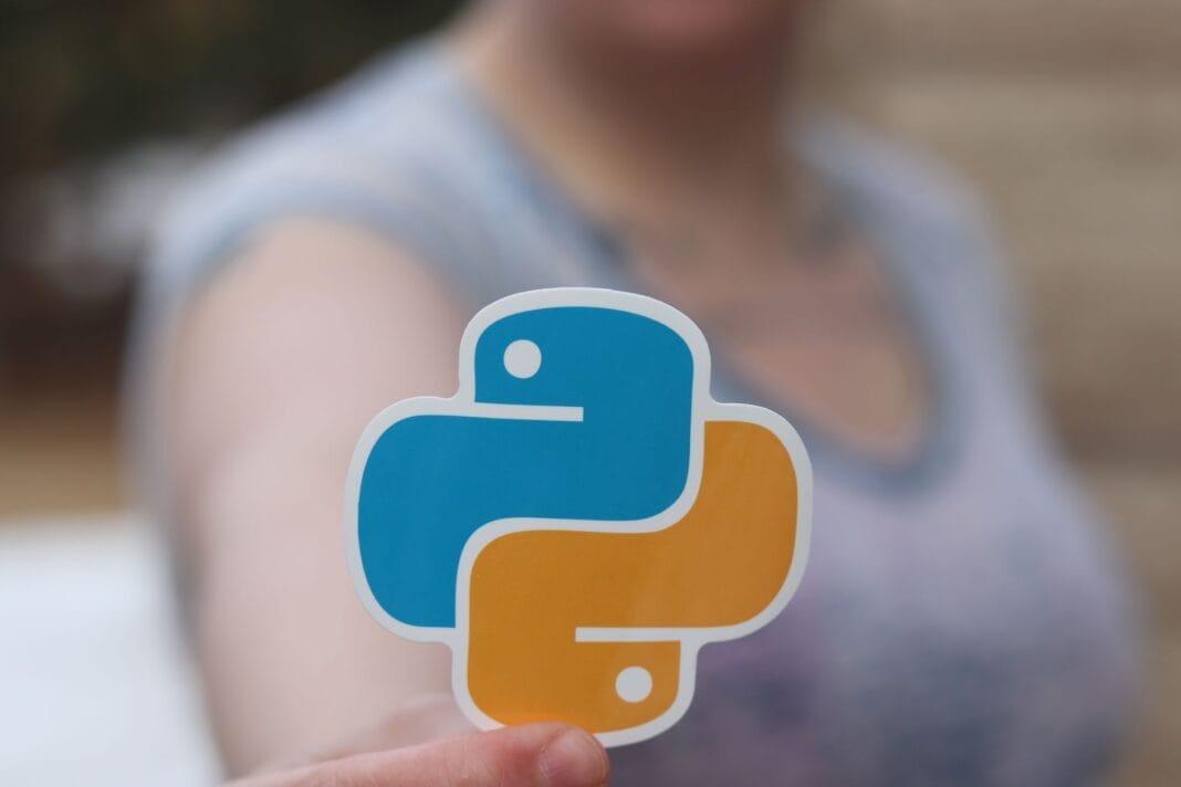 Dłoń trzymająca naklejkę z logo Pythona na rozmytym tle