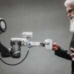 Praktyczne zastosowania sztucznej inteligencji w małej firmie: od automatyzacji zadań po analizę danych Starszy mężczyzna odbiera kubek od ramienia robota w nowoczesnym biurze
